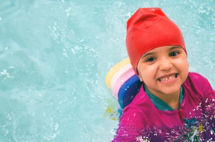 A preschool-aged child smiles in the pool during YMCA swim lessons.