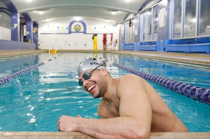 Man with cap and goggles smiling as he starts to swim at North Brooklyn YMCA's indoor pool